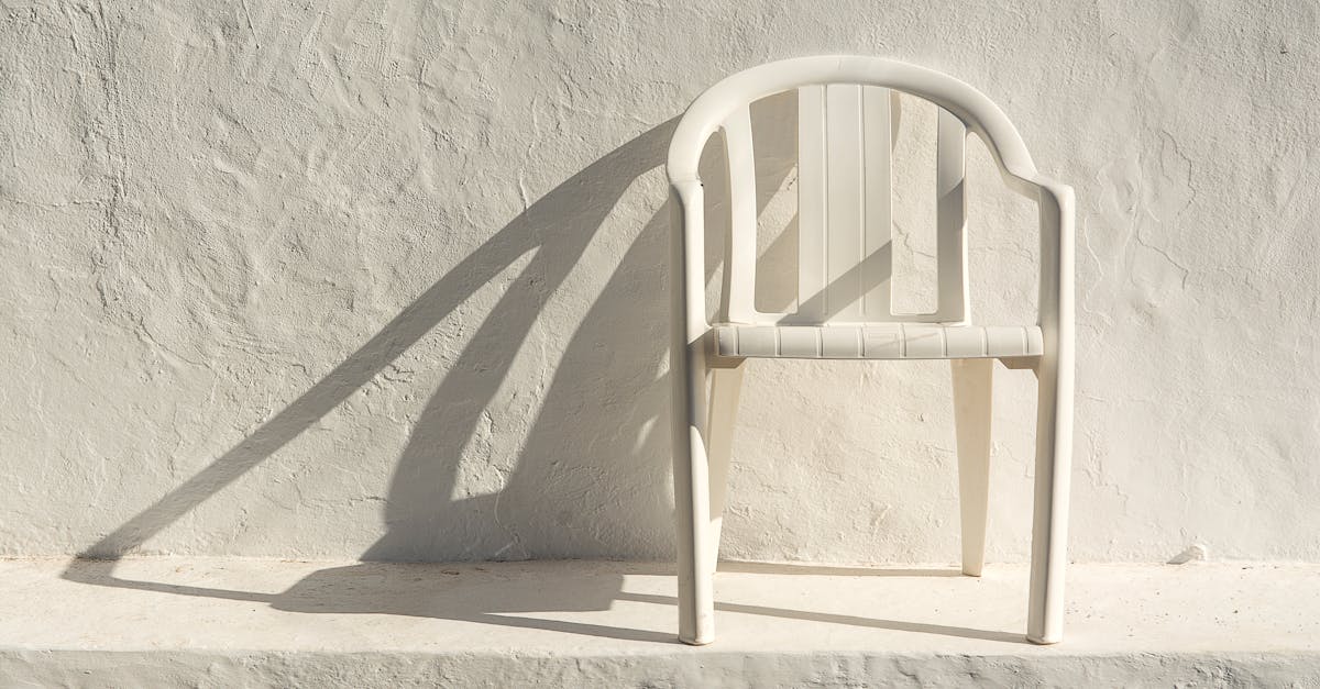 a white plastic chair casting a shadow against a sunlit textured wall